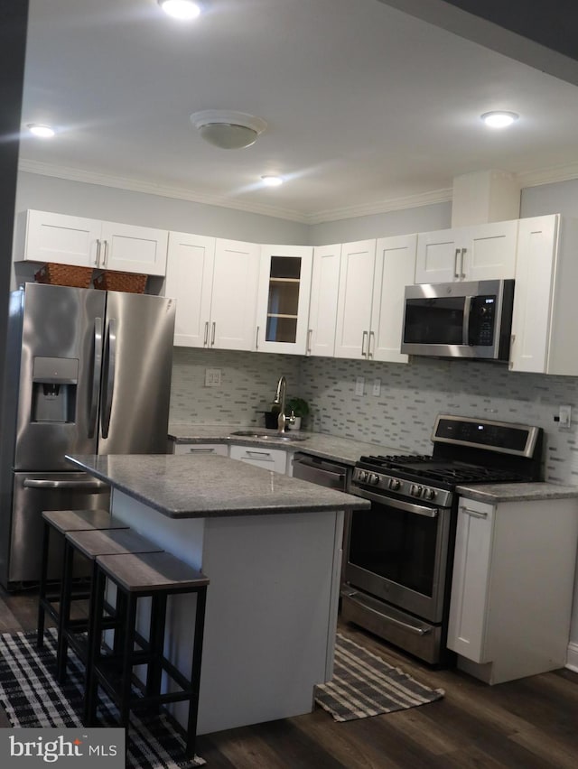 kitchen with a kitchen bar, stainless steel appliances, sink, white cabinets, and a kitchen island