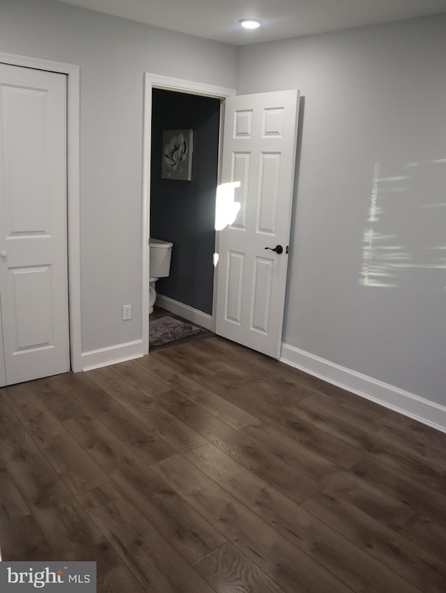 unfurnished bedroom featuring ensuite bathroom and dark wood-type flooring