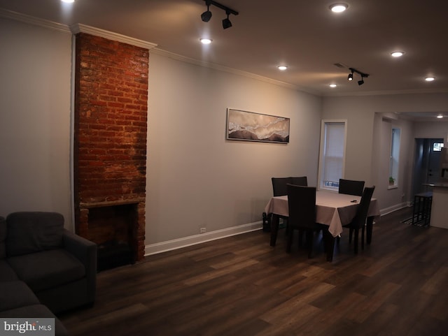 dining room with rail lighting, dark hardwood / wood-style floors, a brick fireplace, and crown molding