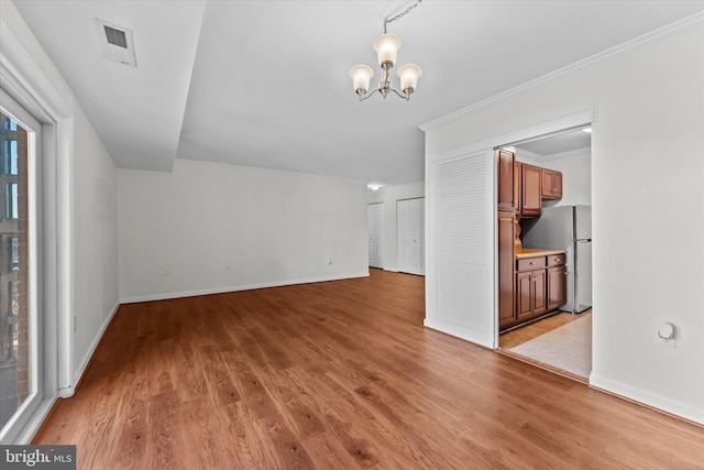 unfurnished living room with light hardwood / wood-style flooring, ornamental molding, and an inviting chandelier