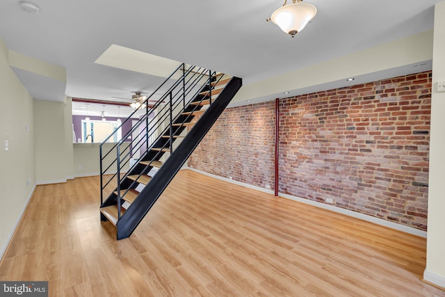 stairs with hardwood / wood-style floors, ceiling fan, and brick wall