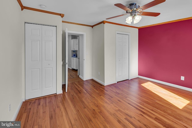 unfurnished bedroom with hardwood / wood-style flooring, ceiling fan, ornamental molding, and multiple closets