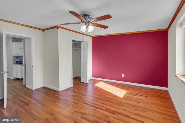 unfurnished bedroom with ceiling fan, a spacious closet, crown molding, hardwood / wood-style floors, and a closet