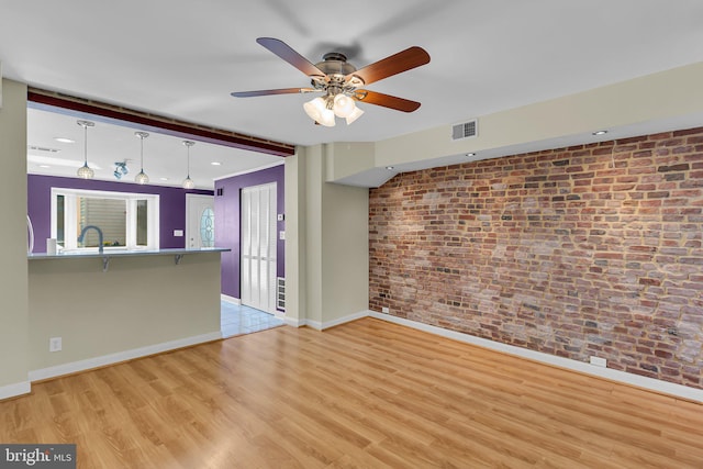 unfurnished living room featuring ceiling fan, brick wall, and light hardwood / wood-style flooring