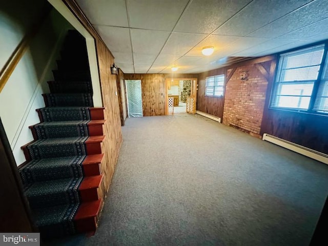 basement with baseboard heating, wood walls, and carpet flooring