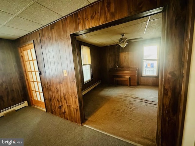 interior space with ceiling fan, baseboard heating, wooden walls, and carpet flooring