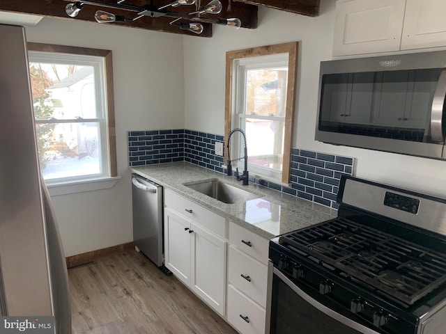 kitchen featuring light stone countertops, appliances with stainless steel finishes, white cabinetry, sink, and backsplash