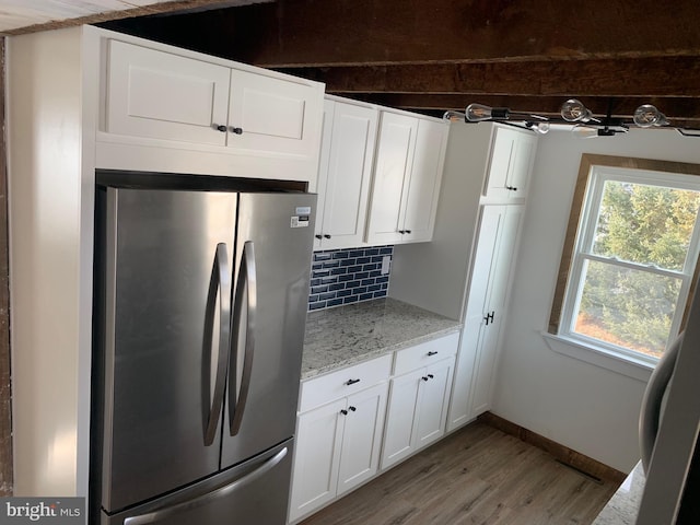 kitchen featuring light stone countertops, stainless steel refrigerator, white cabinets, light hardwood / wood-style flooring, and backsplash