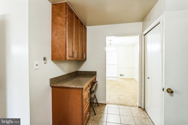 kitchen with brown cabinetry, light colored carpet, and light tile patterned floors