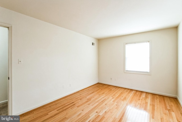 empty room with baseboards, visible vents, and hardwood / wood-style floors