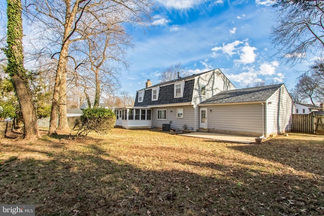 back of property featuring fence, a sunroom, a gambrel roof, a lawn, and a patio area