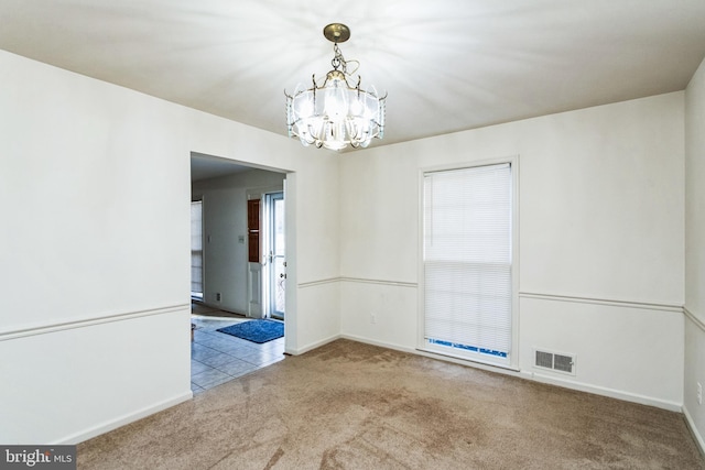 empty room featuring carpet flooring, visible vents, baseboards, and an inviting chandelier