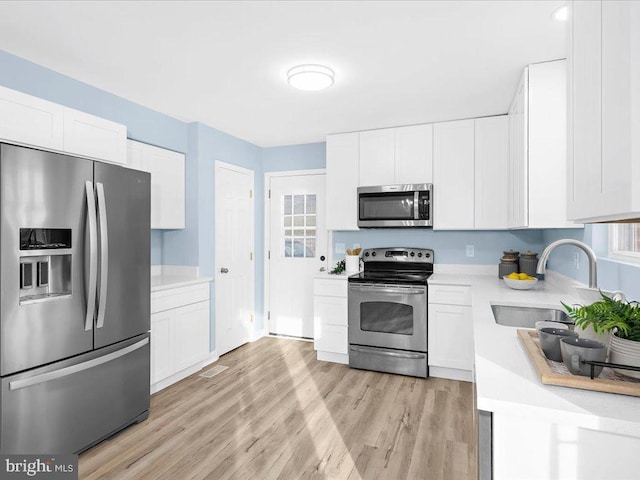 kitchen featuring stainless steel appliances, light countertops, white cabinets, a sink, and light wood-type flooring