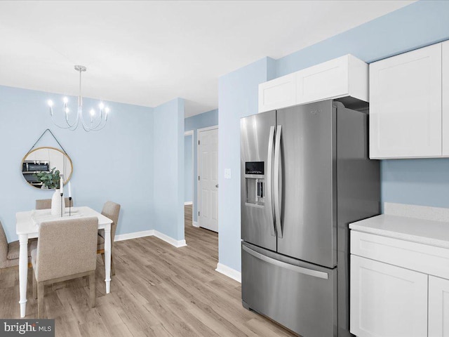 kitchen with white cabinets, light countertops, light wood-type flooring, stainless steel refrigerator with ice dispenser, and decorative light fixtures