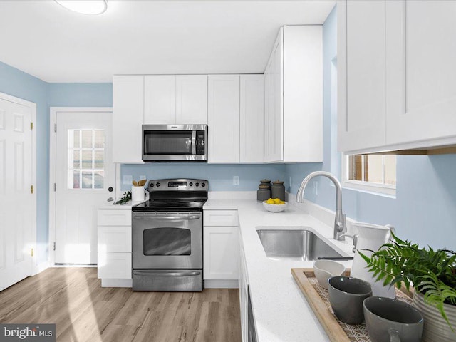 kitchen with stainless steel appliances, light countertops, light wood-style flooring, white cabinets, and a sink