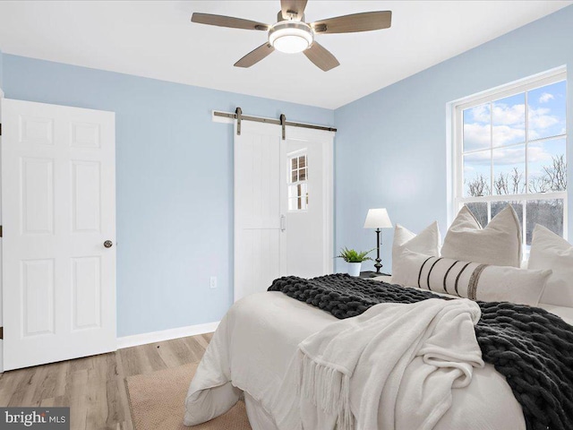 bedroom with ceiling fan, a barn door, light wood-type flooring, and baseboards