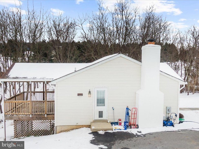 snow covered rear of property with a chimney and a wooden deck