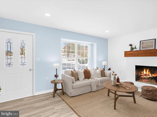 living area featuring a brick fireplace, light wood-style flooring, baseboards, and recessed lighting