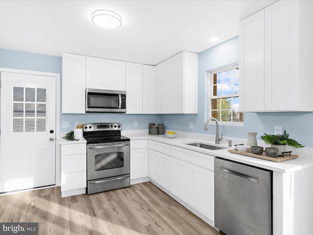 kitchen featuring light wood finished floors, white cabinets, stainless steel appliances, light countertops, and a sink