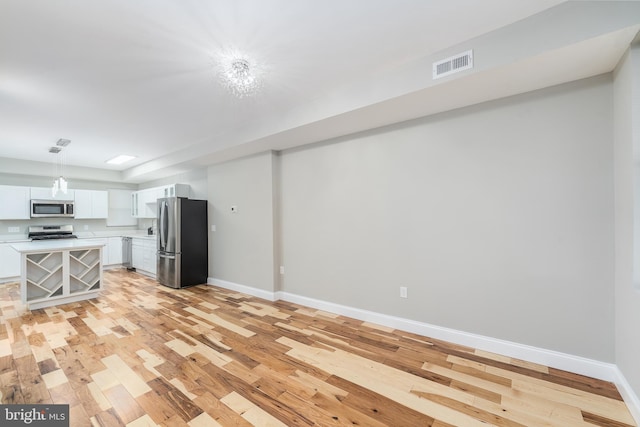 kitchen with appliances with stainless steel finishes, pendant lighting, white cabinetry, and light hardwood / wood-style flooring