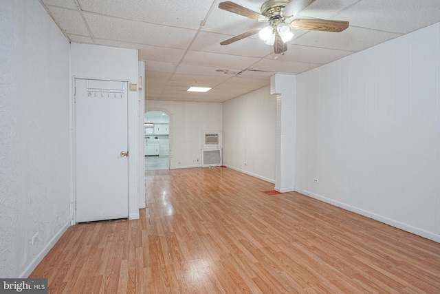 empty room with a wall mounted AC, ceiling fan, a drop ceiling, and light hardwood / wood-style floors