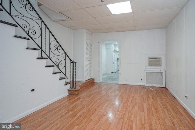 unfurnished living room featuring a drop ceiling, light wood-type flooring, and an AC wall unit