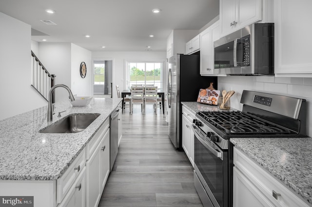 kitchen with stainless steel appliances, white cabinetry, sink, and light stone counters