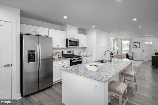 kitchen with a breakfast bar, sink, appliances with stainless steel finishes, a kitchen island with sink, and white cabinets