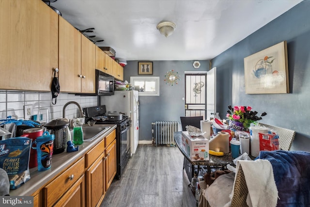 kitchen with radiator heating unit, sink, backsplash, dark hardwood / wood-style flooring, and black appliances