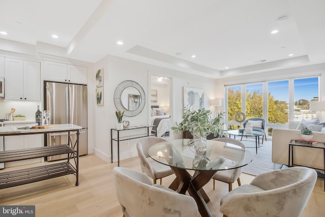 dining area with light wood-type flooring and a tray ceiling