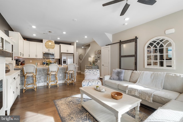 living room with a barn door, ceiling fan, and dark wood-type flooring