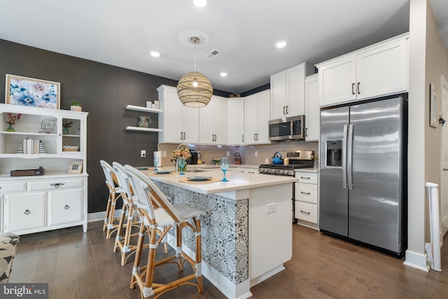 kitchen featuring kitchen peninsula, appliances with stainless steel finishes, a breakfast bar, white cabinetry, and hanging light fixtures