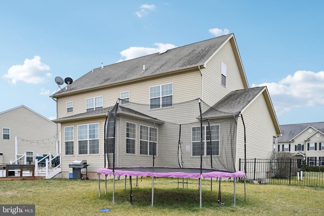 back of property featuring a lawn, a wooden deck, and a trampoline