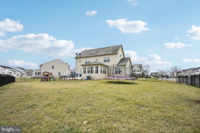 rear view of property featuring a playground, a lawn, and a trampoline