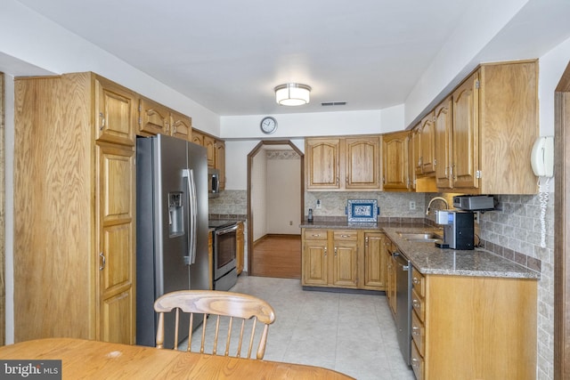 kitchen with appliances with stainless steel finishes, backsplash, dark stone counters, and sink