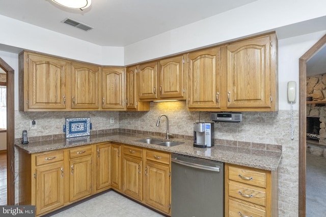 kitchen with backsplash, stainless steel dishwasher, sink, light tile patterned floors, and stone countertops