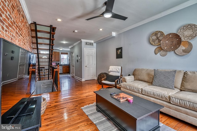 living room with dark wood-type flooring, ornamental molding, ceiling fan, and brick wall