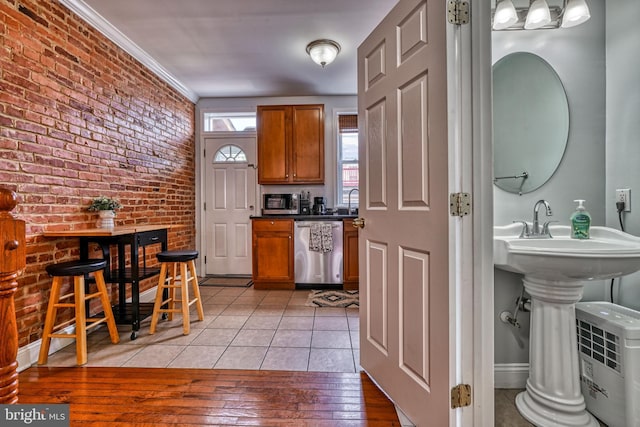 kitchen featuring sink, appliances with stainless steel finishes, ornamental molding, brick wall, and light hardwood / wood-style floors