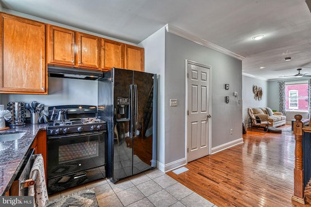 kitchen with dark stone countertops, light tile patterned floors, ceiling fan, black appliances, and crown molding