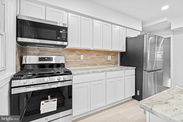 kitchen featuring decorative backsplash, white cabinetry, light stone counters, and appliances with stainless steel finishes