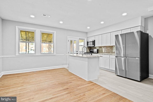 kitchen with stainless steel appliances, light stone counters, light hardwood / wood-style floors, decorative backsplash, and white cabinets