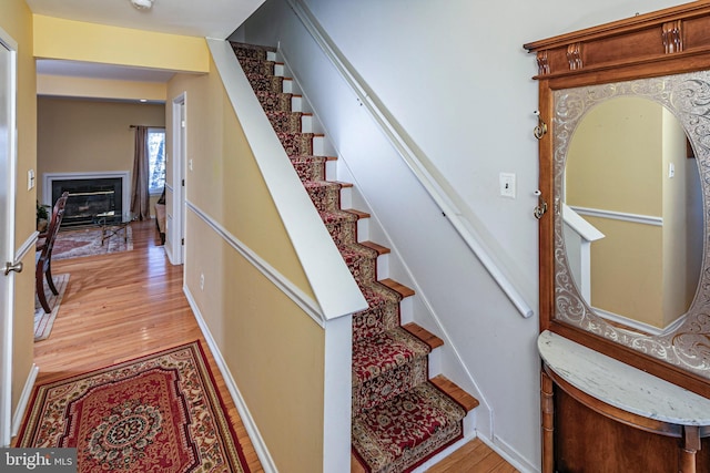 stairway with a high end fireplace and wood-type flooring