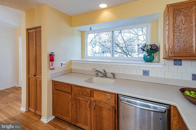 kitchen featuring backsplash, dishwasher, sink, and light hardwood / wood-style flooring