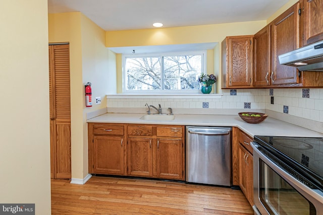 kitchen featuring decorative backsplash, appliances with stainless steel finishes, light wood-type flooring, sink, and range hood