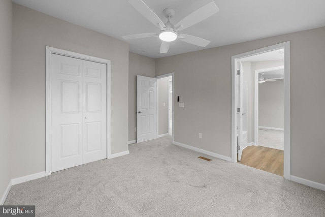 unfurnished bedroom featuring light colored carpet, ensuite bath, a closet, and ceiling fan