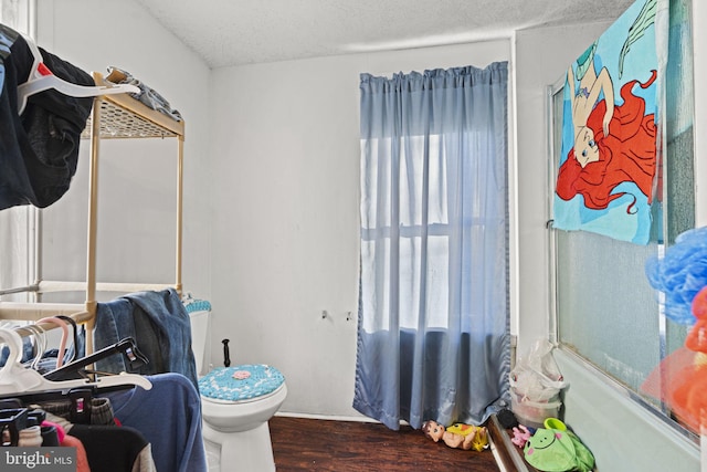 bathroom featuring combined bath / shower with glass door, a textured ceiling, hardwood / wood-style flooring, and toilet