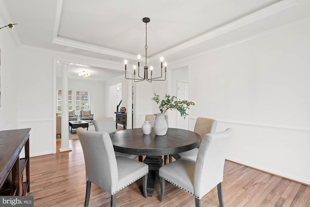 dining area with light wood-type flooring, ornate columns, crown molding, and a raised ceiling