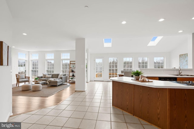 kitchen featuring stainless steel gas stovetop, black dishwasher, sink, lofted ceiling with skylight, and light tile patterned floors