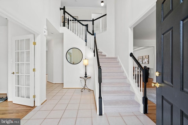 foyer with light tile patterned flooring, crown molding, and a towering ceiling