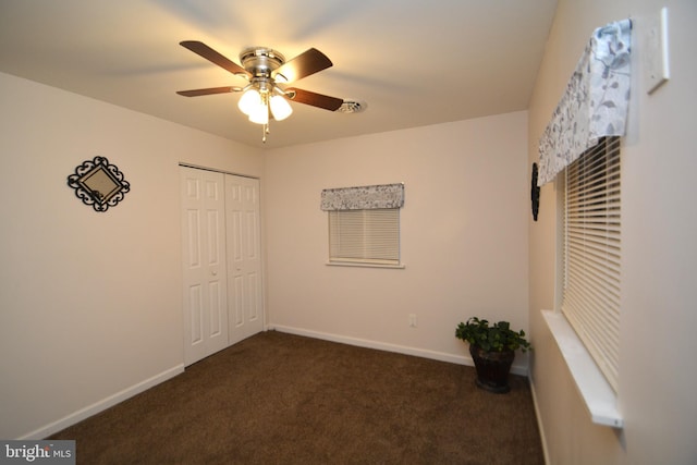 unfurnished bedroom featuring ceiling fan, dark carpet, and a closet